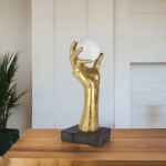 Escultura Mão em resina dourada com bola de Vidro decorativa. Com um design arrojado, esta mão dourada  segurando uma bola de vidro é uma peça super diferenciada. Com altura de 36 cm por 13,5 cm de profundidade e 13,5 cm de largura.