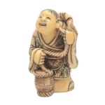 Netsuke em marfim policromado, representando pescador segurando cesto e carregando peixe nas costas. 5 x 2 cm.