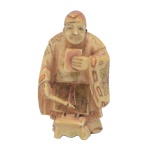 Netsuke em marfim policromado, representando professor explicando aos alunos à frente uma pintura inspirada pelo poema que ele está lendo. 5 x 1 cm.