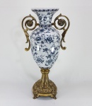 Grande ânfora em porcelana decorada com flores e folhagens em tons de azul, estrutura em metal dourado, alças cinzeladas com folhas de Acanto e terminadas em cabriolés. Med. 50 cm