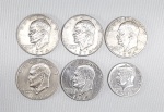 Lote com 6 moedas americanas, sendo cinco (5) de 'One Dollar' e uma de 'Half Dollar'. Datas e materiais variados.