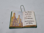 Placa decorativa na forma de livro, descrevendo idades da mulher em italiano, em cerâmica. Medindo 13,5cm x 10,5cm. Leve bicado.