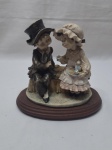 Escultura de casal sentado em resina com base em madeira. Medindo 21cm x 12cm de base x 19cm de altura.