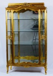Vitrine dourada em estilo francês com entalhes de flores. Interior com 3 prateleiras de vidro e fundo revestido com espelho. Medidas: 98 cm x 45 cm. Altura: 167 cm.