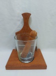 Kit para caipirinha, sendo uma tábua para cortes, um coqueteleira e um socador, sob suporte em madeira. Medindo a coqueteleira 11cm x 12,5cm de altura.