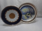 Lote de 2 pratos decorativos em porcelana, sendo um azul cobalto com ouro e um com estampa de casa no fio com friso ouro (desgaste no friso). Medindo o maior 30cm de diâmetro.