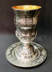 Taça / cálice judaica para Kidush no Shabat em metal prateado com inscrições em hebraico e interior em vermei. Acompanha presentoir, possui marca ART@ na base da taça e no presentoir. Altura de 15 cm e base de 8 cm. Presentoir com 13,5 de diâmetro.