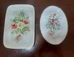 Duas bandejas pequenas em porcelana pintadas à mão, sendo a bandeja oval em porcelana Smith na cor branca decorada no centro com delicadas flores, e a outra sem marcação com pintura de flores no centro - Medidas: 2x10x14 cm e 2x10x15 cm