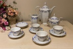 EPIAG, Czechoslovakia - Art Deco 1930 - Aparelho de café incompleto, contendo 6 pires, 4 xícaras, 1 cremeira, 1 açucareiro e um bule, em porcelana esmaltada na cor branca, bordas decoradas com flores em tom azul e filetes em ouro. Marcado e numerado no verso - Alturas: 21 cm ( bule), 13 cm ( açucareiro), 12 cm ( cremeira)