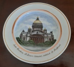 Prato decorativo de porcelana com bordas douradas e, ao centro, uma imagem representando a Catedral de Santo Isaac, localizada em São Petersburgo, Rússia. Este prato é uma peça elegante que combina a delicadeza da porcelana com a sofisticação do dourado, tornando-se uma excelente opção para decoração de interiores. Assinado  no verso - Diâmetro: 18 cm