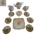 Guarnição para chá em porcelana Inglesa Tuscan Bone China decorada com flores verdes e ramagem dourada sobre fundo branco marcado na base composto de: 1 bule, 1 cremeira, 1 açucareiro, 1 bowl, 1 prato para bolo e 12 xícaras para café com pires, 1 delas com fio de cabelo, Total: 16 peças.