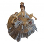 Escultório em porcelana CapodiMonte representando dama sentada em sofá com vestimenta rendada petrificada, Alt. 7, Com. 8 cm.