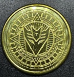 Transformers - Medalhão Original DOURADO do parque da Universal Studios (Estados Unidos) - Emblema dos Deceptcons A imagem reversa em todas as moedas é a mesma. Tem o logotipo NEST Transformers no centro, Universal Studios na parte superior e algumas informações de direitos autorais nas laterais e na parte inferior.- FC