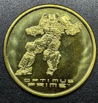 Transformers - Medalhão Original DOURADO do parque da Universal Studios (Estados Unidos) - Optimus Prime. A imagem reversa em todas as moedas é a mesma. Tem o logotipo NEST Transformers no centro, Universal Studios na parte superior e algumas informações de direitos autorais nas laterais e na parte inferior.- FC