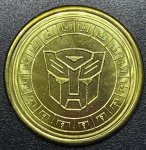 Transformers - Medalhão Original DOURADO do parque da Universal Studios (Estados Unidos) - Emblema dos Auto Bots. A imagem reversa em todas as moedas é a mesma. Tem o logotipo NEST Transformers no centro, Universal Studios na parte superior e algumas informações de direitos autorais nas laterais e na parte inferior.- FC