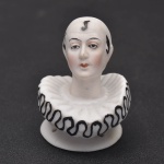 Meia cabeça de boneca -  Esta meia cabeça de boneca Pierrot com gola larga, e franzida está pronta para ser presa a uma esponja de pó. Nesta variação de Pierrot, ele tem um solidéu branco em vez do preto habitual com cachos pretos e  bochechas rosadas. Excelente rosto de Pierrot com olhos delineados em preto, linhas de pálpebras corais, bochechas coradas e lábios vermelhos. Mede 5x4 cm