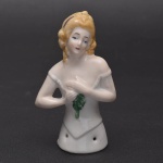 Coleção Half Doll - Notável dama com as mãos juntas sob o peito em expressão contemplativa. Seu vestido é todo branco com o colo a mostra. Cabelos loiros com detalhe em vinho. Base numerada e marcada Germany. Med 10 x 6 cm.