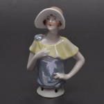 Coleção Half Doll -  Jeitosa mulher com as mão na cintura, bochechas rosadas. Vestimenta azul cintilante com lindo lenço amarelo recaido sob seus ombros. Chapeu modernista na cor laranja. Base marcada Germany e numerada. Mede 10,5 x 7 cm.