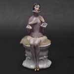 Coleção Half Doll - deslumbrante boneca fielmente Art Deco, estilo e época, com traje lilás , manga e golas brancas muito acentuadas. Cabelos curtos, saia coberta de pó de arroz que pousa tampando  frasco de porcelana onde encontra-se com as pernas finas e elegantes;   vestindo sapatos dourados. Bico de 1 sapato com imperceptivel bicado. Deslumbrante!  Base numerada. Medida total 18,5x8x9,5 cm