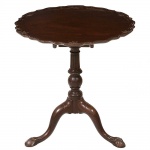 Bela <b>mesa circular </b>inglesa, do período vitoriano, construída em mogno no sistema "tilt top". Tampo de borda movimentada com delicados entalhes floridos. Coluna central em forma de balaústre e três pernas recurvadas terminadas em garras sobre esferas. Primeira metade do séc. XIX. Alt. 70 cm; Diâm. 68 cm