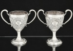 <b>Par de taças com alças laterais </b>em prata Sterling irlandesa do período George III. Bojo em relevos floridos com timbres armoriais em ambas as faces. Base circular. Contraste da cidade de Dublin de 1799 e marca ilegível de prateiro. Peso 790 g. Alt. 18 cm