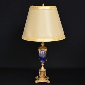 Delicado <B>"abatjour" </b>francês em bronze dourado, com haste montada em cristal, provavelmente BACCARAT, incolor e azul cobalto. Parte superior com cabeças de carneiro e base em pedestal decorado com guirlandas e perolado. Cúpula em seda pirogravada. Séc. XIX. Atl. Total 65 cm