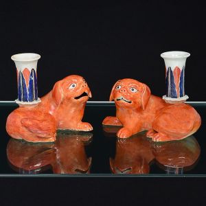 <B>Par de castiçais </b>em porcelana Companhia das Índias, modelados em cães de fó, na cor "rouge de fer". Receptáculos decorados com folhas sobre fundo branco. Séc. XVIII / XIX. Alt. 12 cm; Compr. 15,5 cm