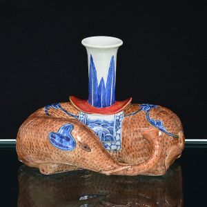 Belo <b>castiçal</b> em porcelana Companhia das Índias policromada em tonalidades de sépia e azul índigo, modelado em figura de elefante. Receptáculo decorado com folhas. Séc. XVIII / XIX. Alt. 13,5 cm; Compr. 19,5 cm