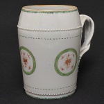 <b>Caneca</b> "mug", em forma de barril, em porcelana Companhia das Índias decorada com reservas floridas em verde, "rouge de fer" e perolados. Alças entrelaçadas. Séc. XVIII. Alt. 16 cm