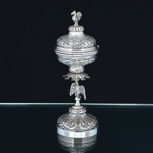 <b>Âmbula </b>em prata brasileira Sterling 925 ml decorada com volutas e concheados. Haste com representação do divino e tampa encimada por figura de ave. Marca na base PPM. Peso 465 g. Alt. 28 cm