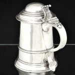 "<b>Tankard</b>" em prata inglesa, do período George III, séc. XVIII. Apresenta bojo liso com frisos, tampa abobadada e alça em "S" terminada em coração. Contraste da cidade de Londres de 1771 e marca do prateiro WALTER BRIND. Peso 690 g. Alt. 20 cm