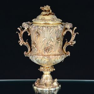 Belíssima <b>taça troféu </b>em prata "vermeil", inglesa do período William IV, ricamente repuxada e cinzelada com volutas e flores em relevo. Na face anterior reserva cercada por cavalos e alegorias do turfe no topo. Inscrições: Richmond Races - 1833. Lord Viscount Falkland - George Hartley Esq: RIE - STEWARDS. As alças são em curvas e contracurvas modeladas com os motivos do bojo. Base em ondulações e pega da tampa com modelado de uvas e folhas de parreira. Contraste da cidade de Londres de 1833 e marca do prateiro JBGCWN. Peso 4.000 g. Alt. 44 cm