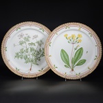 <b>Par de travessas circulares</b> em porcelana dinamarquesa da importante manufatura Royal Copenhagen modelo "Flora Danica". Cada peça, inteiramente pintada à mão em belíssima policromia com suas designações botânicas e numeração no verso. Apresenta borda em mínimos picotados cobertos a folha de ouro. Diâm. 36 cm