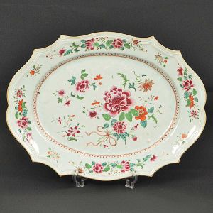 Grande <b>travessa oblonga </b>em porcelana Companhia das Índias decorada em policromia nos esmaltes da Família Rosa com peônias e flores de lótus entre ramagens. Bordas recortadas e filetadas. Séc. XVIII. Mínimo bicado no verso. Med. 47 x 35 cm