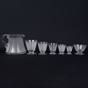 Maison BACCARAT - <b>Conjunto de copos</b> de baixa estatura em cristal francês lavrado com losangos em "satiné". Marca da "cristallerie" no verso. Constando de jarra, 6 taças p/ champanhe, 14 copos p/ água, 4 copos p/ vinho tinto, 3 copos p/ vinho branco, 8 copos p/ vinho do Porto e 12 copos p/ licor. Total de 48 peças. Alt. da jarra 14,5 cm; Alt. do copo de água 10 cm; Alt. da taça de champanhe 6,5 cm