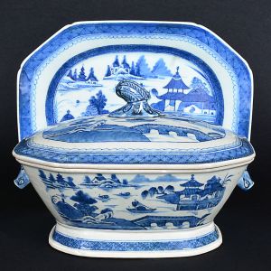 <b>Sopeira de forma oblonga e cantos chanfrados e seu "presentoir"</b> em porcelana Companhia das Índias, dita Macau. Apresenta decoração em azul índigo "underglaze" com paisagem lacustre, pagodes e embarcações. Pegas do bojo modeladas em cabeças de lebres e da tampa em estilização vegetal. Séc. XVIII. Compr. do "presentoir" 35,5 cm; Compr. da sopeira 31 cm