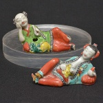 Pequeno <b>par de estatuetas </b>em porcelana Companhia das Índias representando casal com bebê em posição de descanso. Período Jiaqing. No verso selo de Goffi Carboni - Roma. Compr. 9 cm