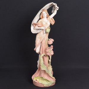 Grande <b>estatueta </b>Art Nouveau em porcelana tcheca "Royal Dux" policromada em tonalidade de rosa e verde claro, representando figura de ninfa com flores e folhas. Alt. 88 cm