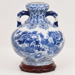 Robusto <b>vaso </b>bojudo em porcelana chinesa decorada em azul índigo "underglaze" com figuras de aves entre belas composições floridas. Bocal chanfrado e alças modeladas em cabeças de animais fabulosos. Séc. XIX / XX. Acompanha base em madeira. Alt. 36 cm