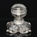 <b>Tinteiro </b>em prata europeia, "Sterling", repuxada e moldada no formato de capacete medieval. Viseira móvel revelando interior com recipiente. Apresenta contrastes e marca de prateiro. Peso 235 g. Alt. 12 cm