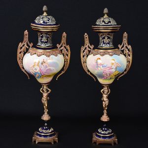 <b>Par de ânforas </b>em faiança francesa ao gosto das porcelanas de Sèvres apresentando forma bojuda decorada em policromia romântica. Montagem em bronze e hastes moldadas com figuras infantis. Tampas encimadas por pinhas. Alt. 66 cm