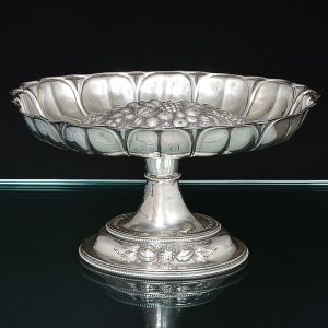 <b>Fruteira de pé</b>, de forma oval, em prata inglesa vitoriana. Parte superior de borda gomada, decorada ao centro com frutos em relevo. Parte externa com "crest" e monograma. Haste e base perolados. Contraste da cidade de Sheffield de 1848 e marca de prateiro. Peso 585 g. Alt. 15 cm; Compr. 27,5 cm