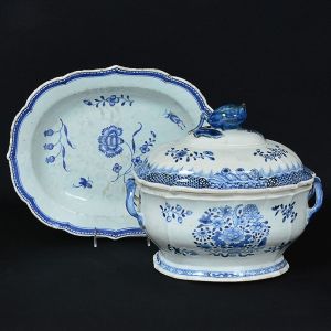 Elegante <b>sopeira oblonga com seu "presentoir" </b>em porcelana Companhia das Índias, feita aos moldes dos exemplares europeus do séc. XVIII. Decoração em azul índigo com cartuchos e arabescos floridos sobre fundo branco. Pega da tampa modelada em fruto e borda do "presentoir" em ondulações. Séc. XVIII. Compr. do "presentoir" 37 cm