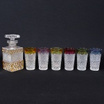 <b>Conjunto de 6 copos para "long drinks" </b>em meio cristal profusamente lapidado em geometrizados com bordas em cores variadas. Um deles com mínimo bicado. Acompanha garrafa (tampa presa). Alt. 22,5 cm