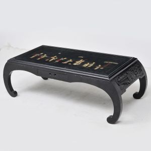 Antiga <b>mesa de centro chinesa </b>em madeira patinada de negro. Tampo envidraçado e decorado por múltiplas figuras em cena de exterior e vestes em pedras diversas. Laterais entalhadas com figuras e pagodes. Med. 38 x 118 x 52 cm