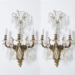 Belíssimo <b>par de apliques para três luzes cada</b>, franceses, em bronze dourado ornamentado com volutas. Eixo central, "bobèches" e pingentes em cristal BACCARAT de diversas formas e lapidações. Séc. XIX. Alt. 86 cm