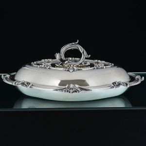 <B>"Entrée Dish"</B>, prato coberto de forma ovalada em prata inglesa do período William IV. Apresenta borda recortada com filete intercalados por estilizações vegetais. Alça destacável com a possibilidade de reversão para duas travessas distintas. Contraste da cidade de Londres de 1835 e marcar parcialmente ilegível de prateiro. Peso 1.790 g. Compr. 35,5 cm