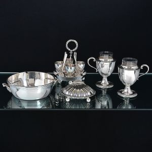 <b>Lote de 5 peças em metal </b>espessurado a prata: a) Porta caviar da Maison Christofle (falta o recipiente de cristal do centro). Diâm. 18,5 cm; b) Porta ovos quentes inglês da casa Mappin & Webb. Alt. 18 cm; c) Porta parmesão em forma de "coquille" da casa Mappin & Webb com recipiente interno em vidro, este com pequenos bicadinhos na borda. Larg. 13 cm; d) Par de porta ovos em metal Elkington com recipiente em vidro. Alt. 14 cm