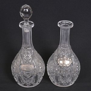 <b>Par de garrafas </b>piriformes (uma faltando a tampa) em cristal francês BACCARAT profusamente lapidado em estilizações geometrizadas. Hastes serrilhadas e tampa multifacetada. Marca da "cristallerie" na base. Acompanha colares em prata. Tampa com bicado na parte interna. Alt. 31 cm