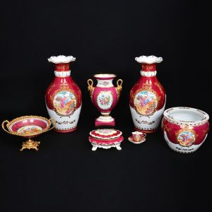 L F Fine Porcelain T Limoges  <b>Conjunto de 7 peças em porcelana </b>decorada com paisagem romana, em policromia com ricos adornos a ouro. Constando de: a) Par de vaso bojudos; b) "Fish bowl"; c) Vaso ao gosto Império; d) Caixa para joias; e) Fruteira; f) Pequena xícara com pires. Origem indefinida. Porcelana de boa feitura, porém acredita-se terem sido fabricadas na China, nos anos 50 e 60. Alt. dos vasos maiores 40,5 cm; Diâm. do "fish bowl" 21,5 cm; Compr. da caixa 17,5 cm